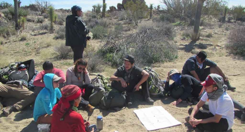 A group of people and their gear rest on the ground, surrounding a map spread out. 